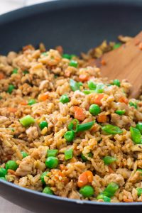 wooden spatula stirring skillet of gluten free turkey fried rice with peas, carrots, and green onions