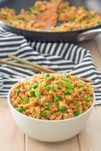 bowl of gluten free turkey fried rice with peas and carrots in a bowl with a skillet in the background