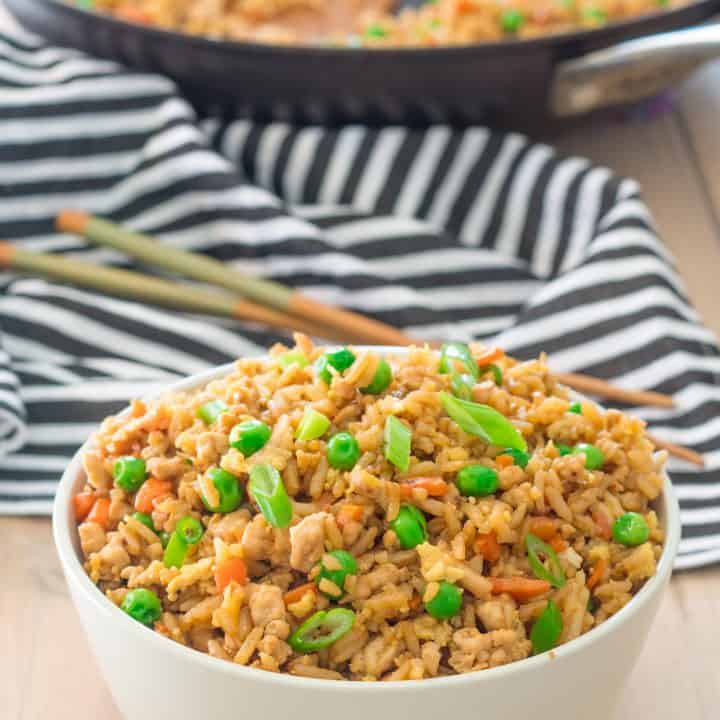 bowl of gluten free turkey fried rice with peas and carrots in a bowl with a skillet in the background