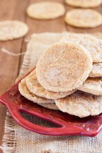 gluten free snickerdoodles on a red ceramic square plate or tray, on a wooden table with some burlap in the background