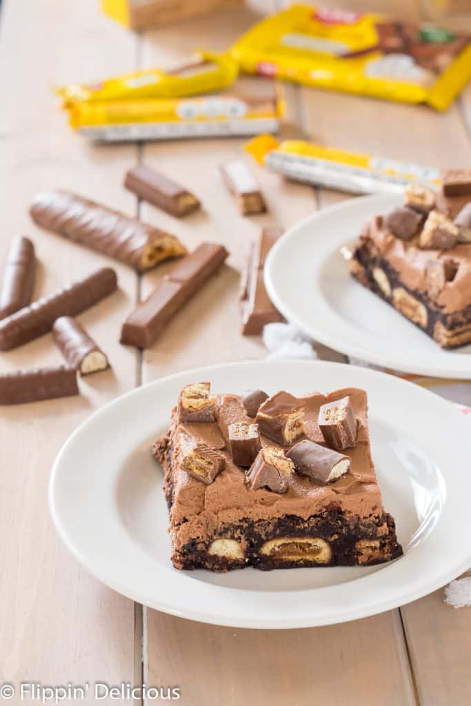 gluten free candy stuffed brownies with chocolate frosting on a white plate with candy bars in the background