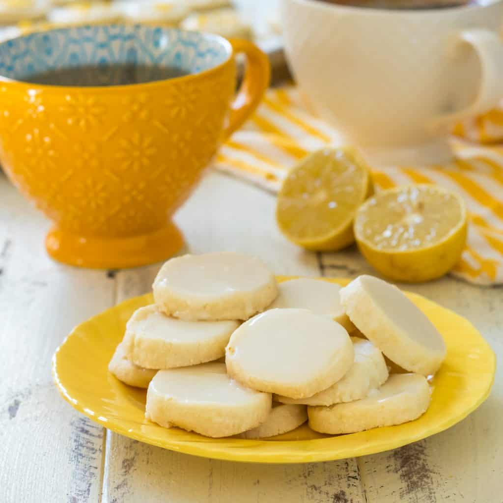 Iced gluten free lemon shortbread on a yellow plate with a yellow tea cup in the background