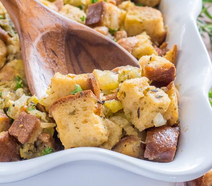 gluten free stuffing with green chile in a white casserole dish with a wooden spoon scooping out a serving