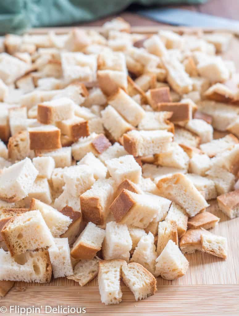 cubes of gluten free bread on a cutting board, being prepared to make gluten free dressing