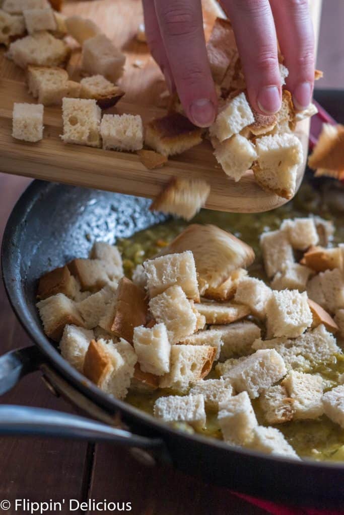 adding cubed gluten free bread to skillet with sauteed onion, celery, garlic, and green chile