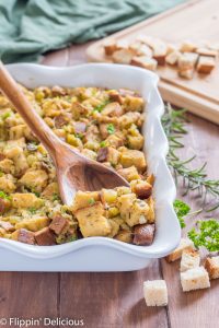 wooden spoon scooping gluten free stuffing with green chile out of a white casserole dish