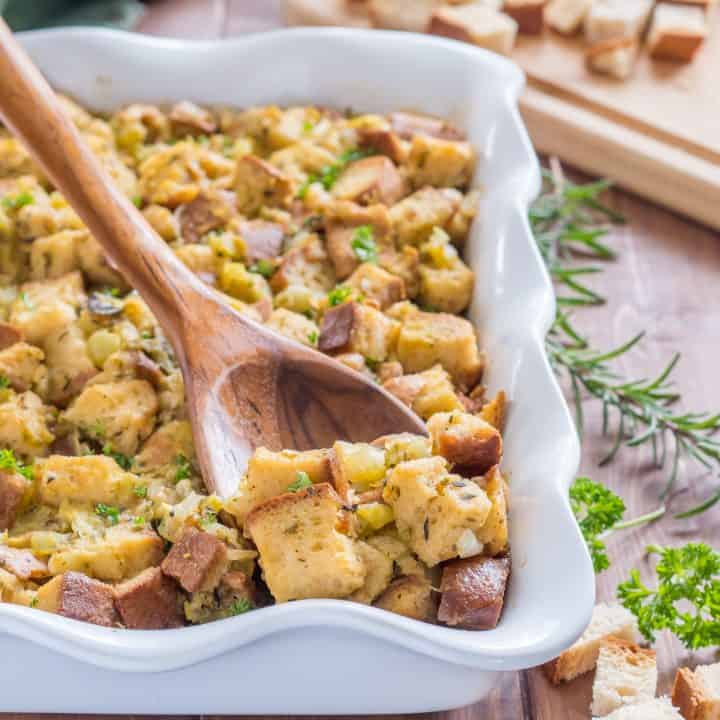 wooden spoon scooping gluten free stuffing with green chile out of a white casserole dish