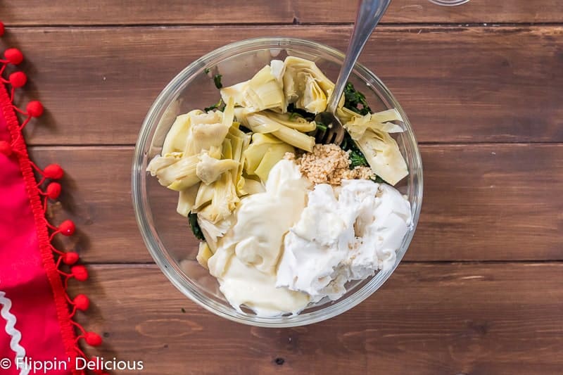 Glass bowl with spinach, artichokes, garlic, lemon juice, dairy free cream cheese, and mayo