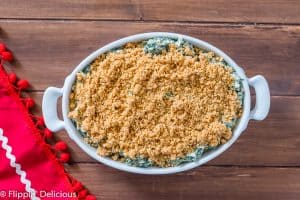 overhead of gluten free spinach artichoke dip with buttered breadcrumbs on top before baking, on wooden table with red tea towel