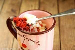 gluten free red velvet mug cake on a fork placed over a mug filled with gluten free red velvet cake and cream cheese frosting for valentines day
