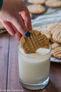 hand holding gluten free peanut butter cookie and dipping it in a glass of milk