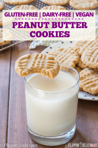 gluten free peanut butter cookie with bite taken out balanced on rim of glass of milk, with a plate full of gluten free peanut butter cookies in the background