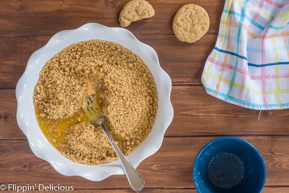 melted vegan butter and gluten free cookie crumbs in a white pie pan