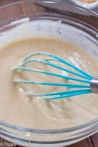 glass bowl full of vegan vanilla pudding being stirred by a teal whisk.