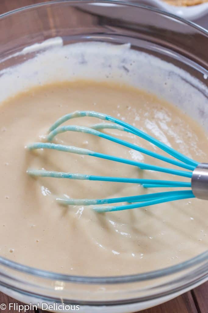 glass bowl full of vegan vanilla pudding being stirred by a teal whisk. 