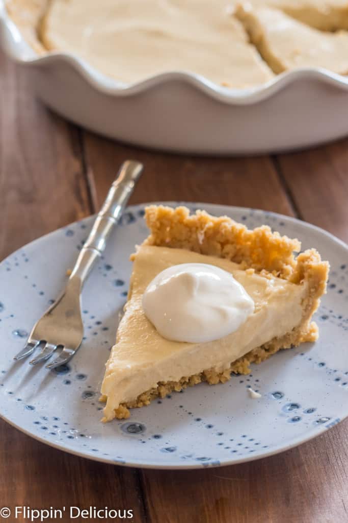 slice of vegan pudding pie ith hipped topping on a blue plate with a small fork on a wooden table
