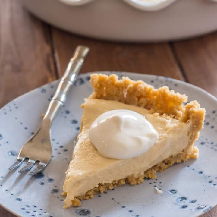 slice of vegan pudding pie ith hipped topping on a blue plate with a small fork on a wooden table