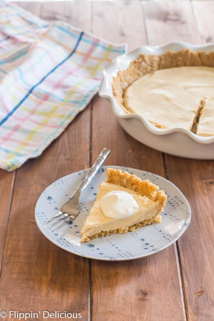 slice of vegan pudding pie on a blue plate topped with whipped topping with a full pie in the background