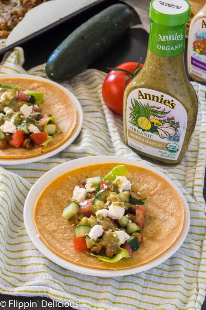 vegetarian chickpea taco with feta, cucumbers, and tomatoes on a white plate with a tomato and cucumber in the background