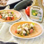 greek vegetarian tacos with chickpeas on a white plate with a green and white dish towel and bottle of annie's dressing