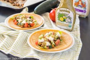 greek vegetarian tacos with chickpeas on a white plate with a green and white dish towel and bottle of annie's dressing