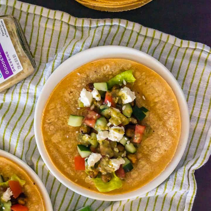 white plate with yellow corn tortilla taco with roasted chickpeas, lettuce, cucumbers, tomatoes, and feta cheese,