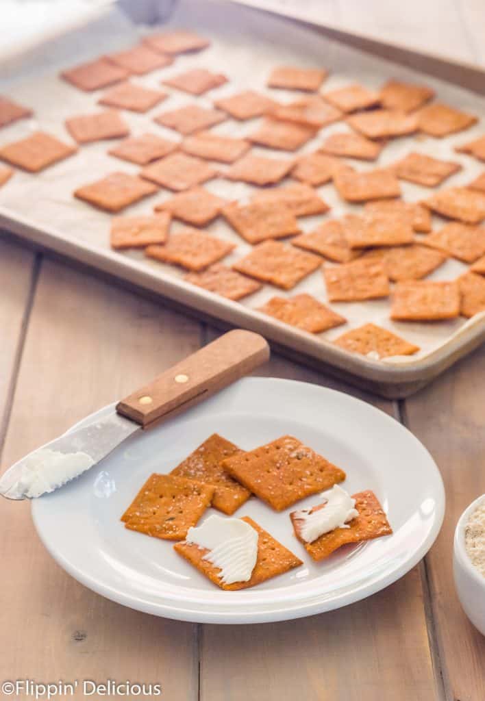 small white plate with five gluten free pizza crackers on it, two spread with cream cheese