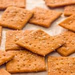gluten free crackers that are pizza flavored, sprinkled with kosher salt, spread out on a sheet of off-white parchment paper