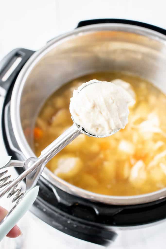 spring loaded scoop full of gluten free dumpling batter over an instant pot with broth, chicken and vegetables