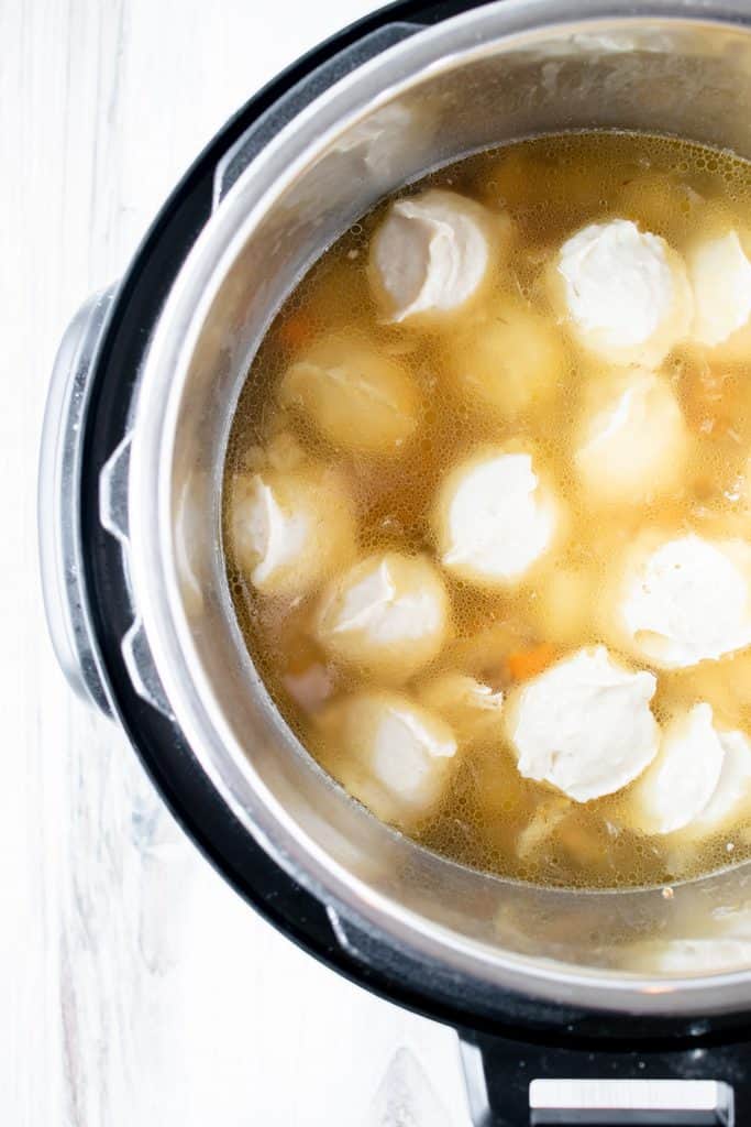 instant pot full of broth with scoops of gluten free dumpling batter floating on the top