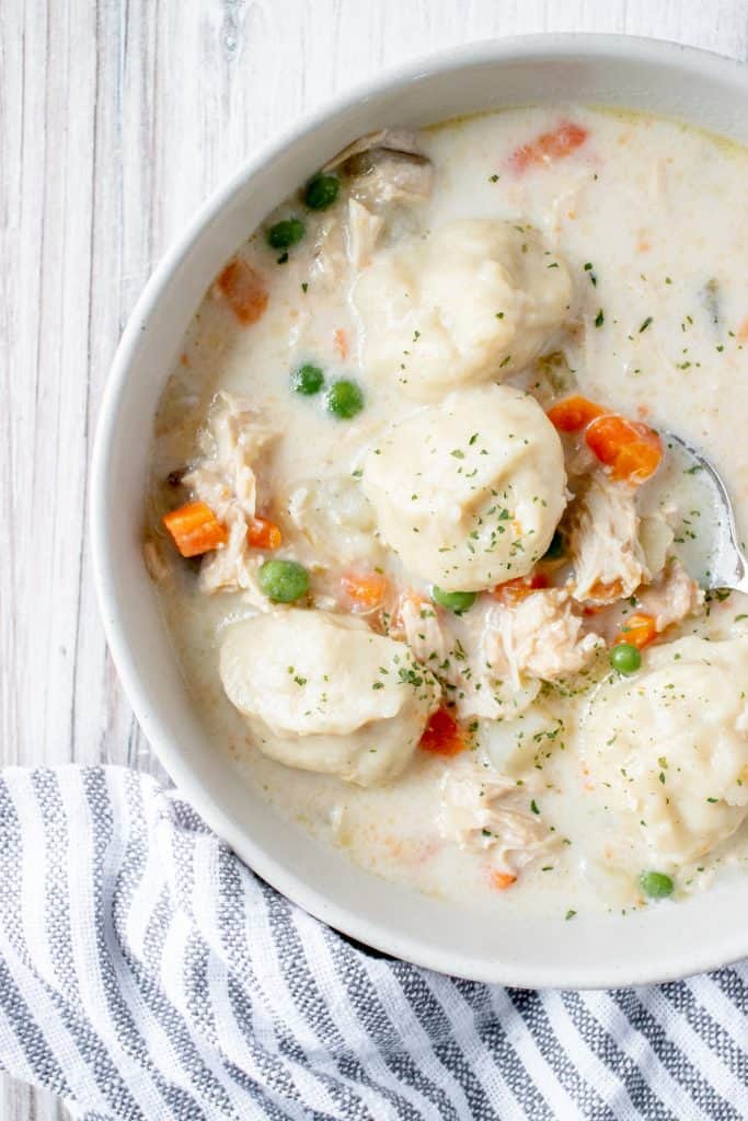 white bowl filled with gluten free chicken and dumpling soup with carrots and peas on a white background