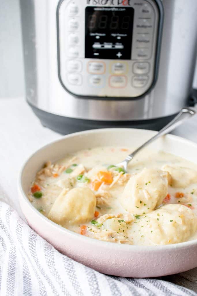 white bowl filled with gluten free chicken and dumplings soup, with a spoon scooping out a gluten free dumpling, with an instant pot pressure cooker in the background