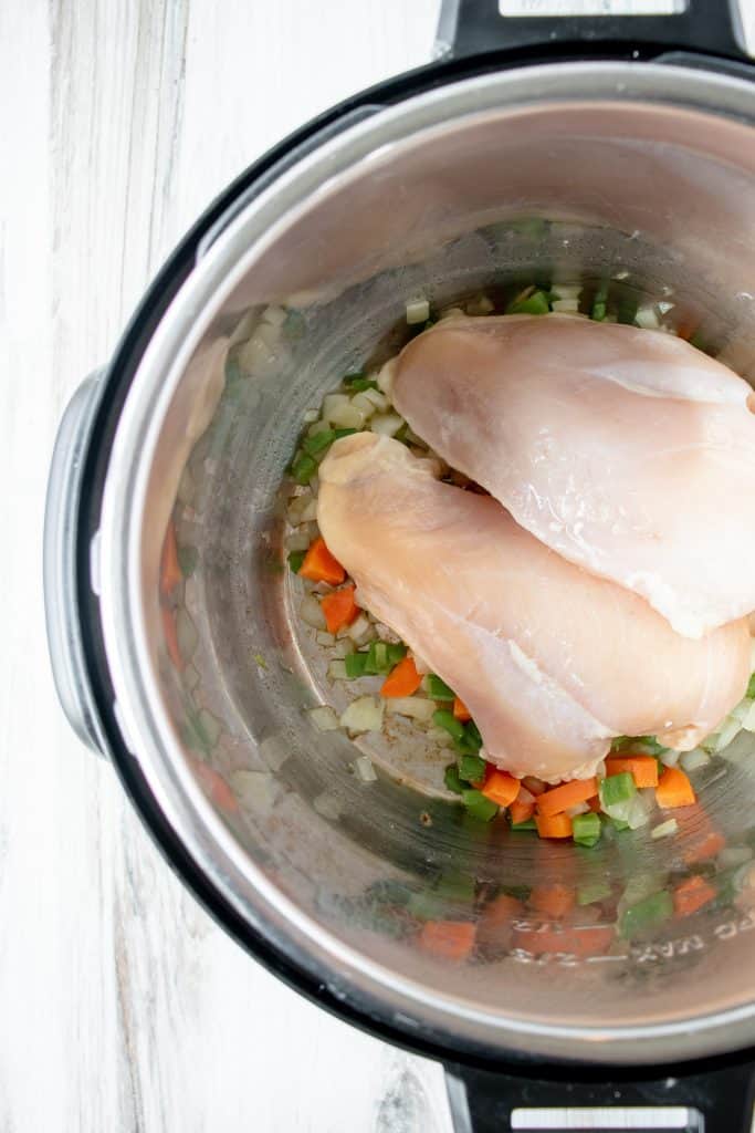 Instant Pot with sauteed carrots, onions, and celery with two chicken breasts placed on top