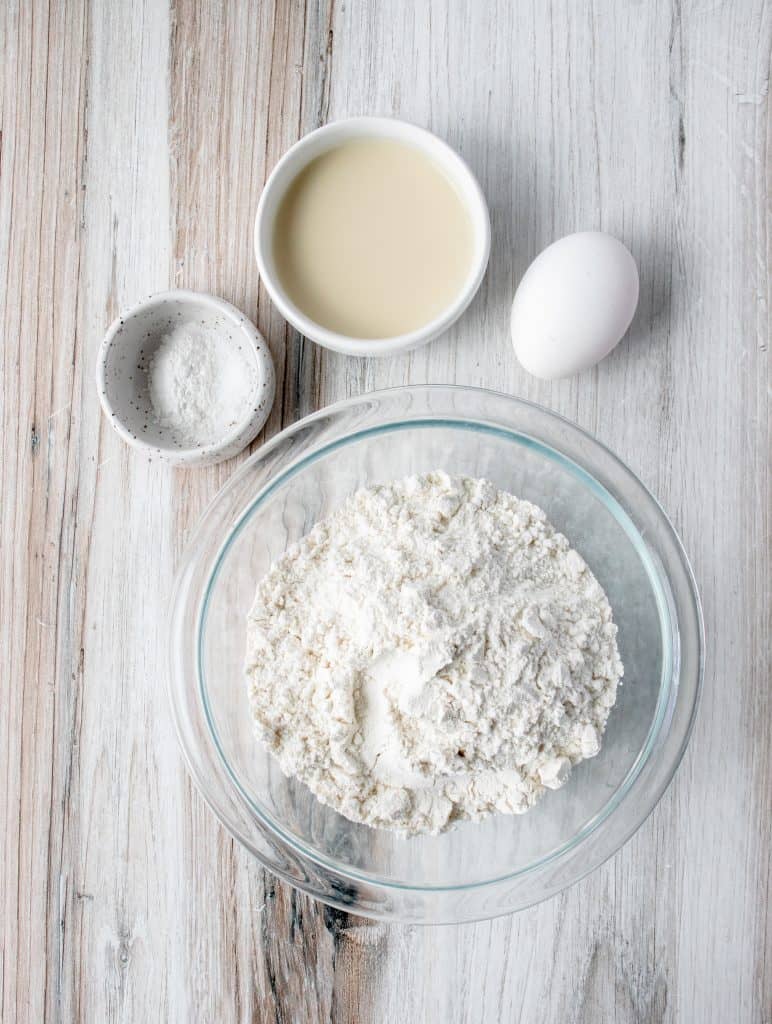 glass bowl with gluten free flour, an egg, white dish with baking powder an salt, and a white dish with dairy free milk 