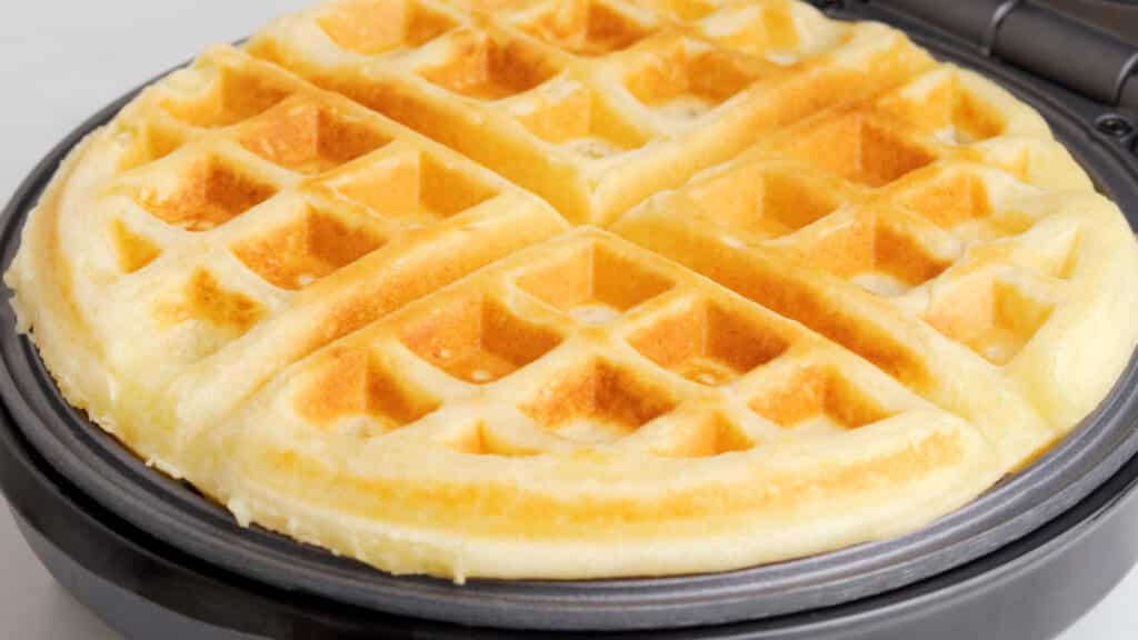 A gluten free waffle, golden brown, ready to come out of a belgian waffle iron