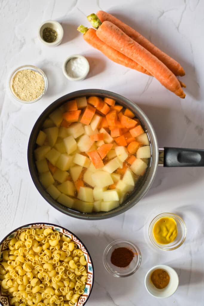 ingredients to make vegan macaroni and cheese sauce, carrots and potatoes steamed in a pan