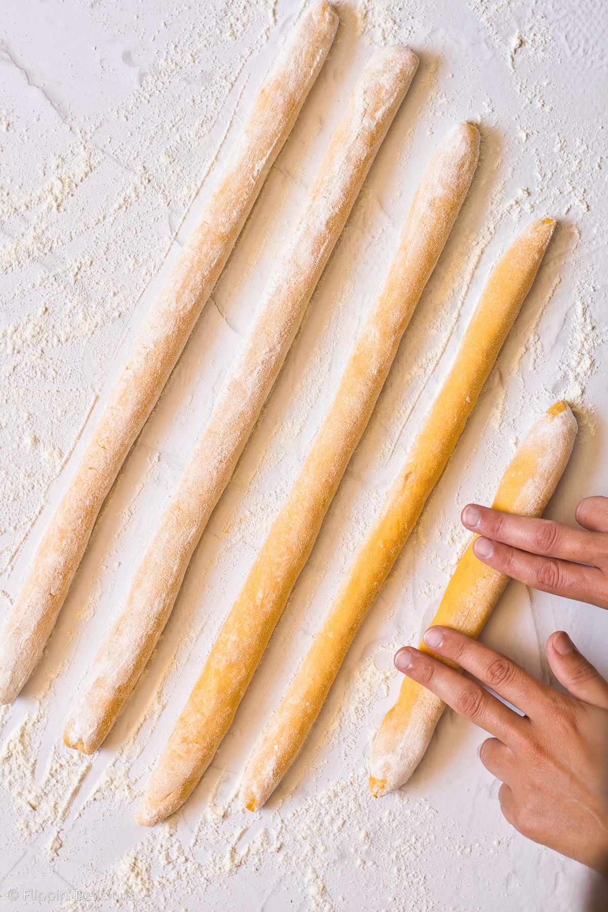 overhead photo of rolling gluten free pumpkin gnocchi dough into snakes in preparation to shape them on a white marble table top sprinkled with flour