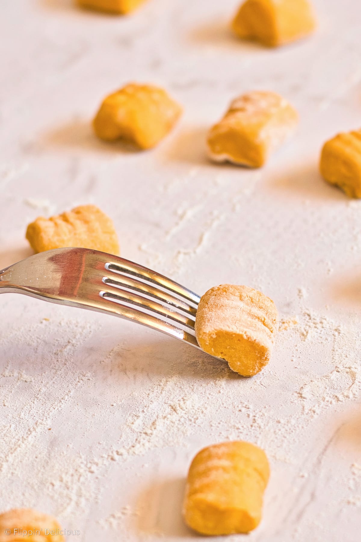 rolling gluten free gnocchi over the upside down tines of a fork, on a white marble floured countertop