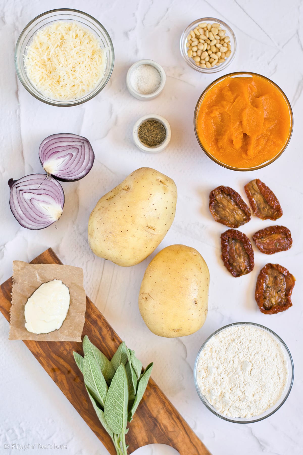 overhead photo of vegan pumpkin gnocchi ingredients; potatoes, pumpkin, salt, gluten free flour, and ingredients for sauce including sundried tomatoes, red onion, pine nuts, and sage, vegan butter, and vegan parmesan cheese