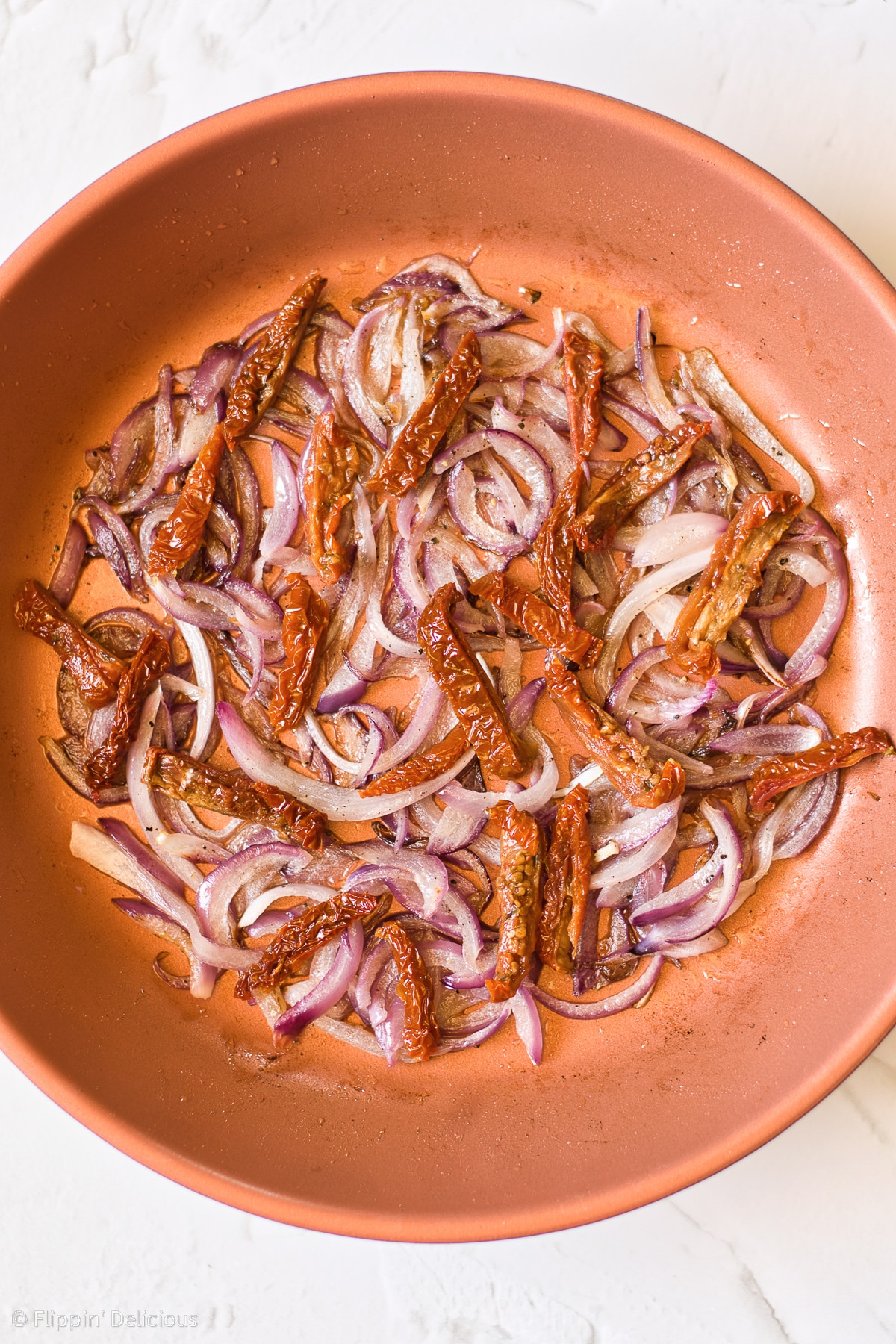 copper pan with onions and sundried tomatoes frying until golden and softened