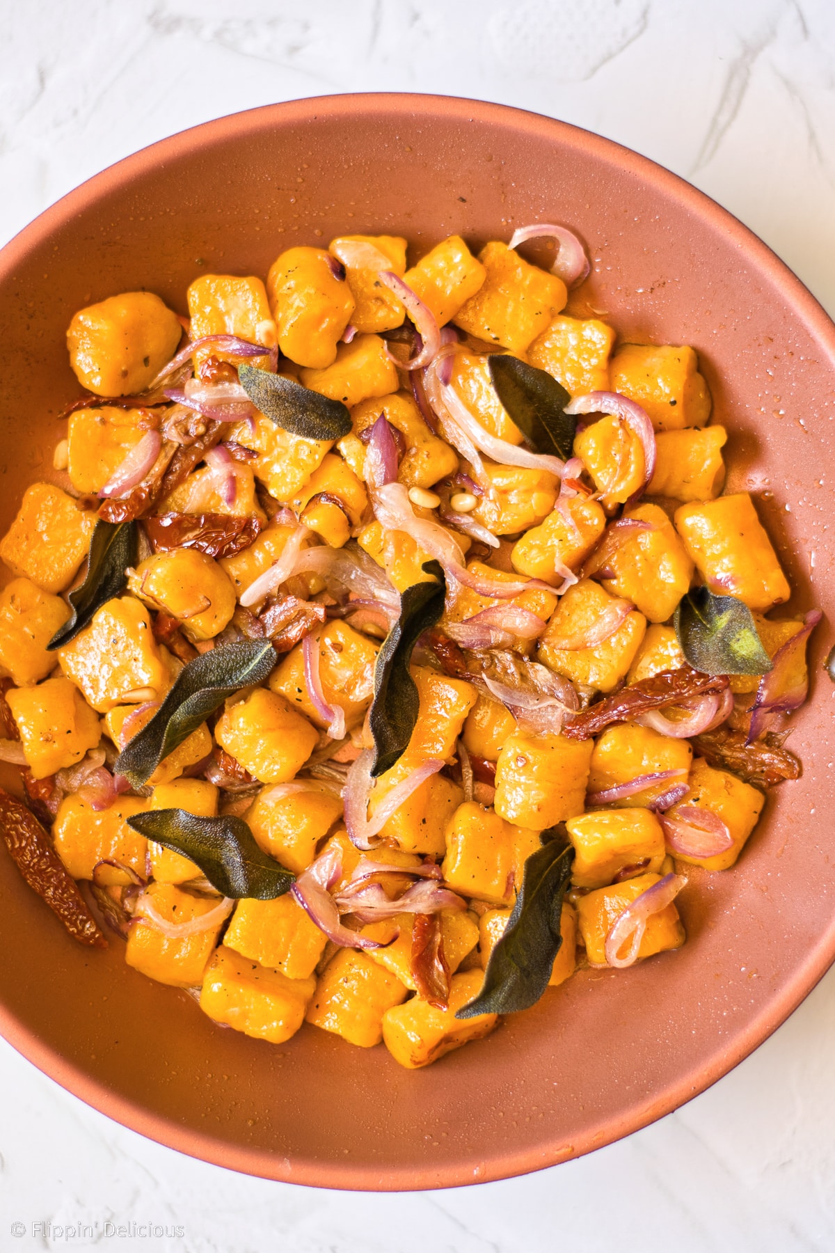 photo of copper frying pan with gluten free vegan pumpkin gnocchi with red onions and fried sage pine nuts and sundried tomatoes
