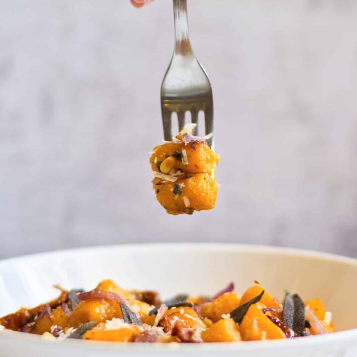 gluten free pumpkin gnocchi on a fork over a bowl filled with gluten free gnocchi