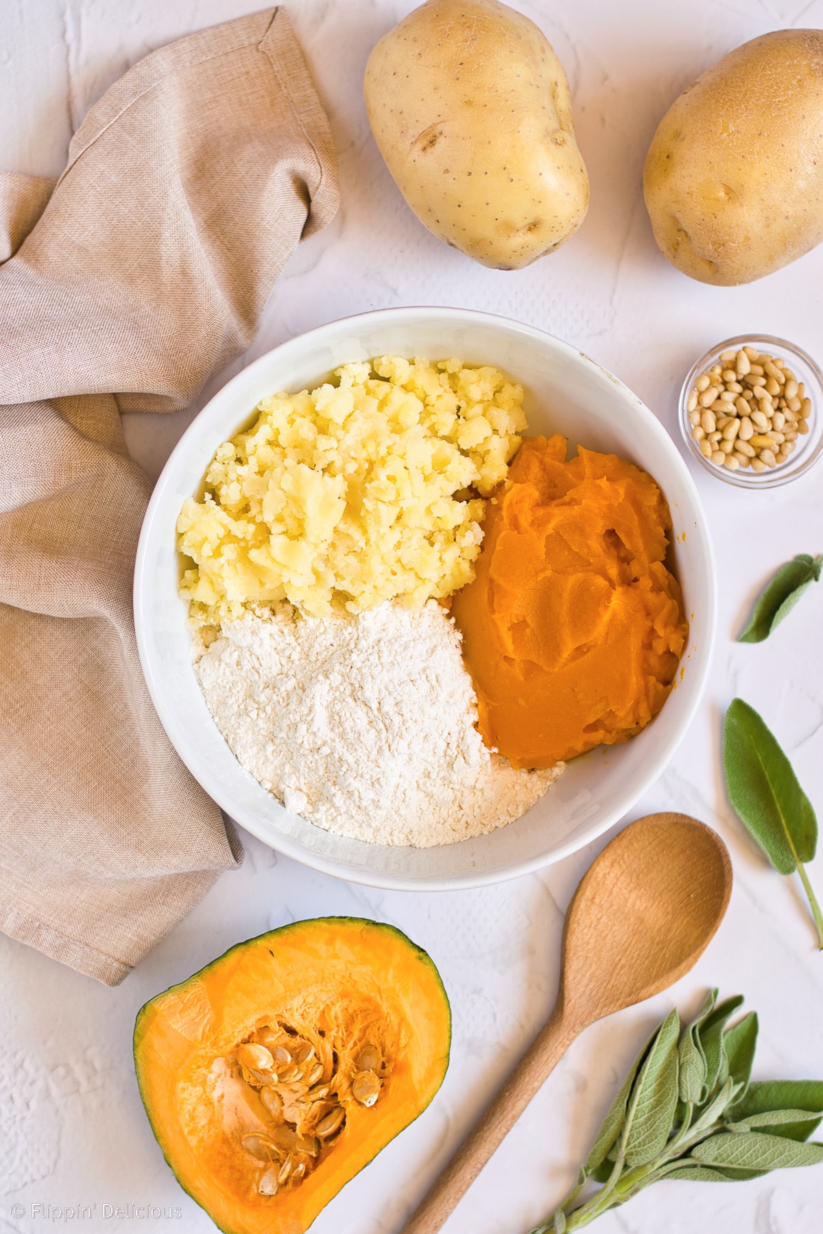 overhead photo of vegan pumpkin gnocchi ingredients; potatoes, pumpkin, salt, gluten free flour, and ingredients for sauce on the white table around