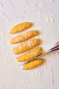 Overhead photo of gnocchi dough on a marble table, cutting it into pieces to shape