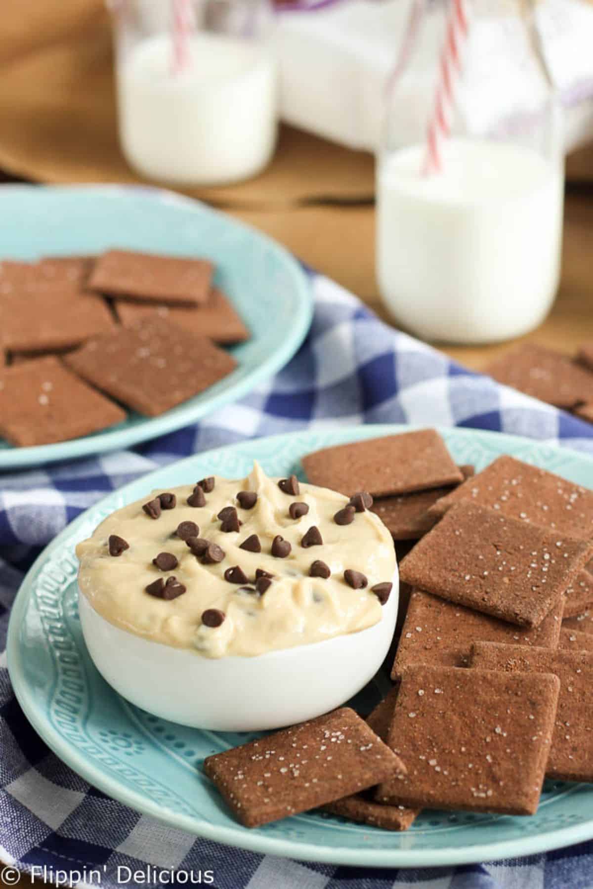 Healthier Gluten-Free Cookie Dough Dip in a small bowl with crackers on a blue plate.