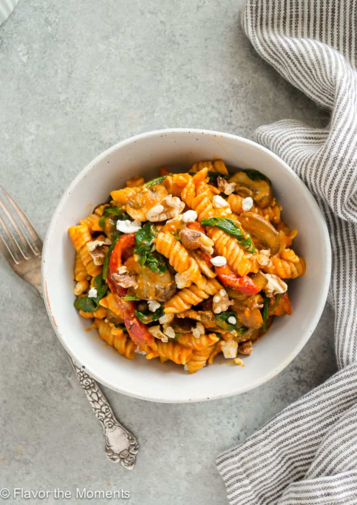 Roasted Red pepper Pasta with Goat Cheese, Mushrooms, and Spinach in a white bowl.