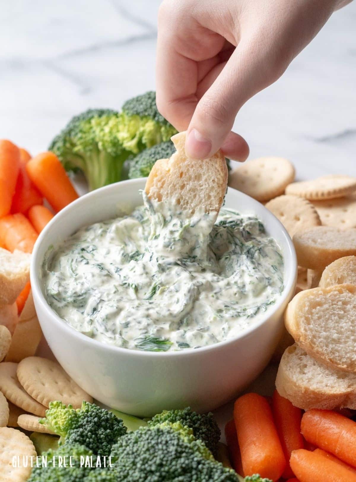 Spinach Dip in a white bowl scooped by a piece of bread.