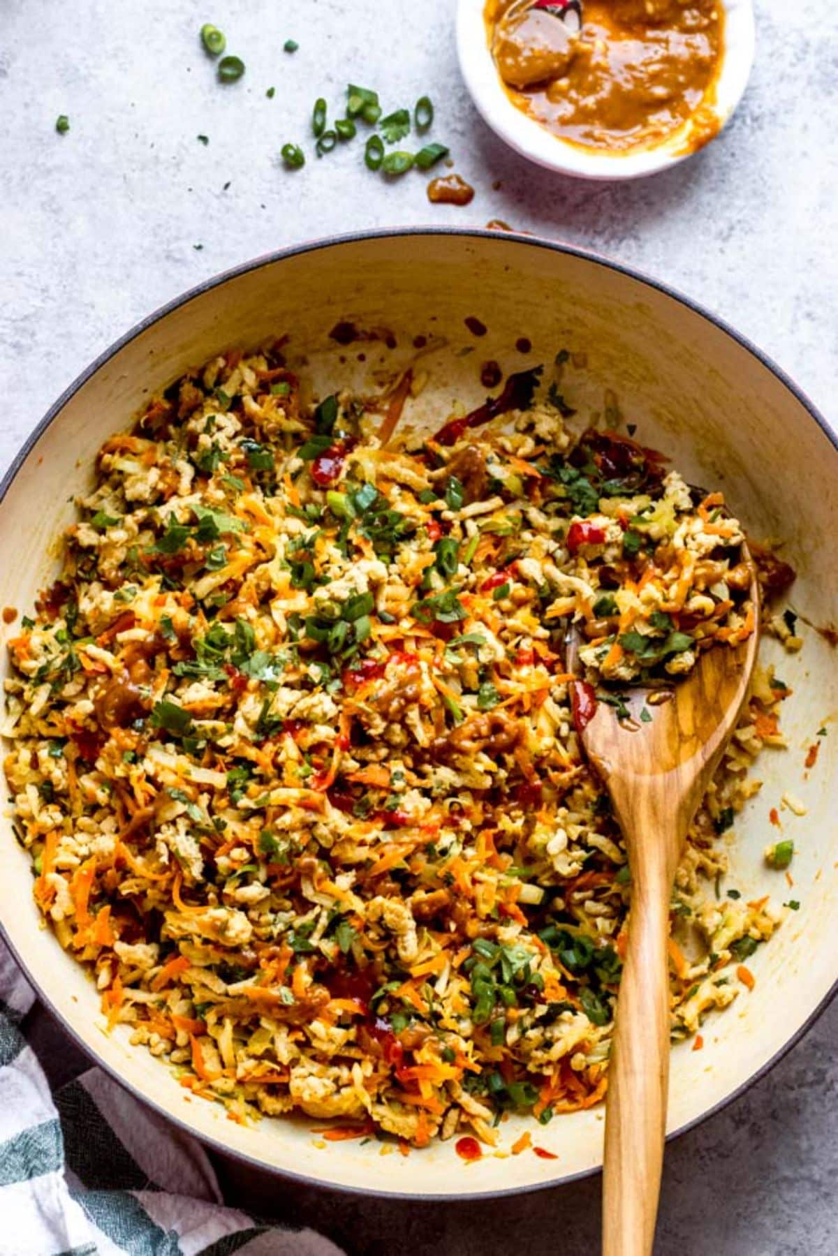 Thai Chicken and Cabbage in a skillet with a wooden spatula.