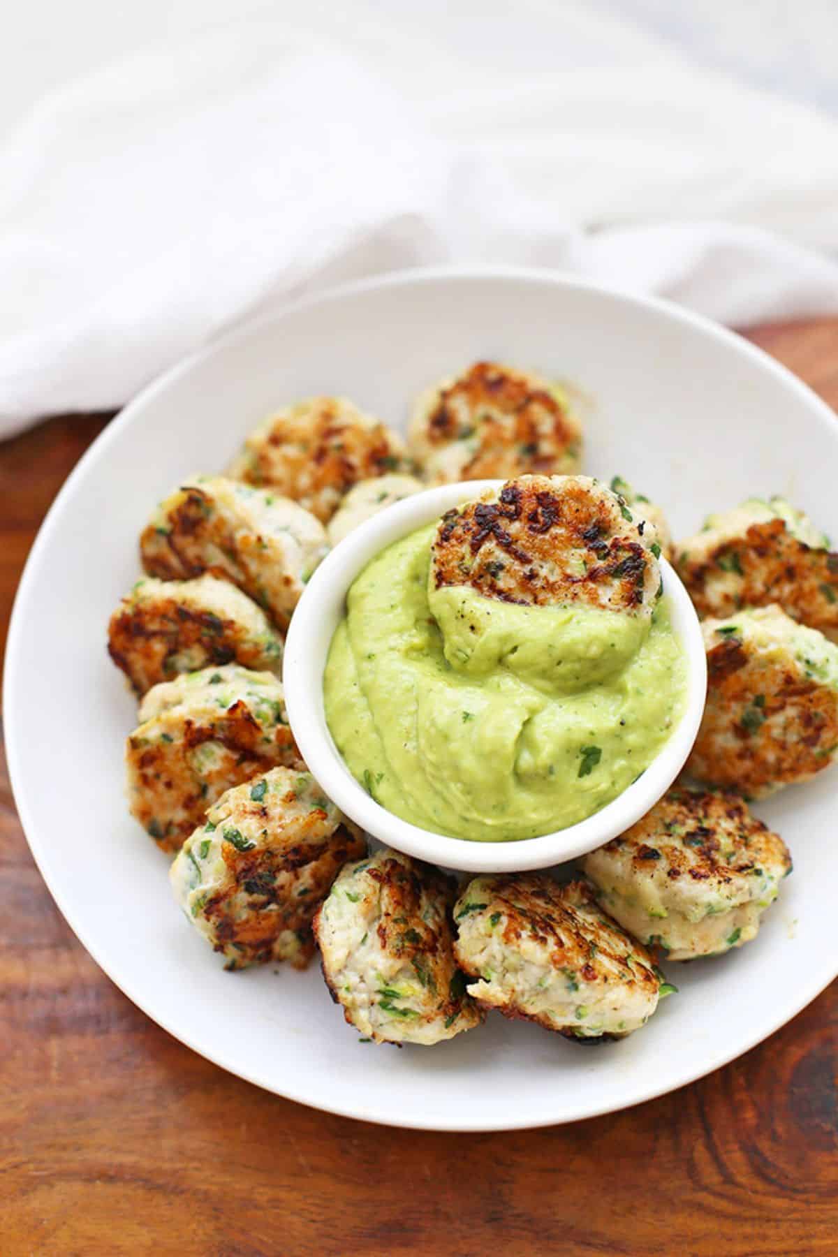 Chicken Zucchini Poppers with a bowl of dip on a white plate.