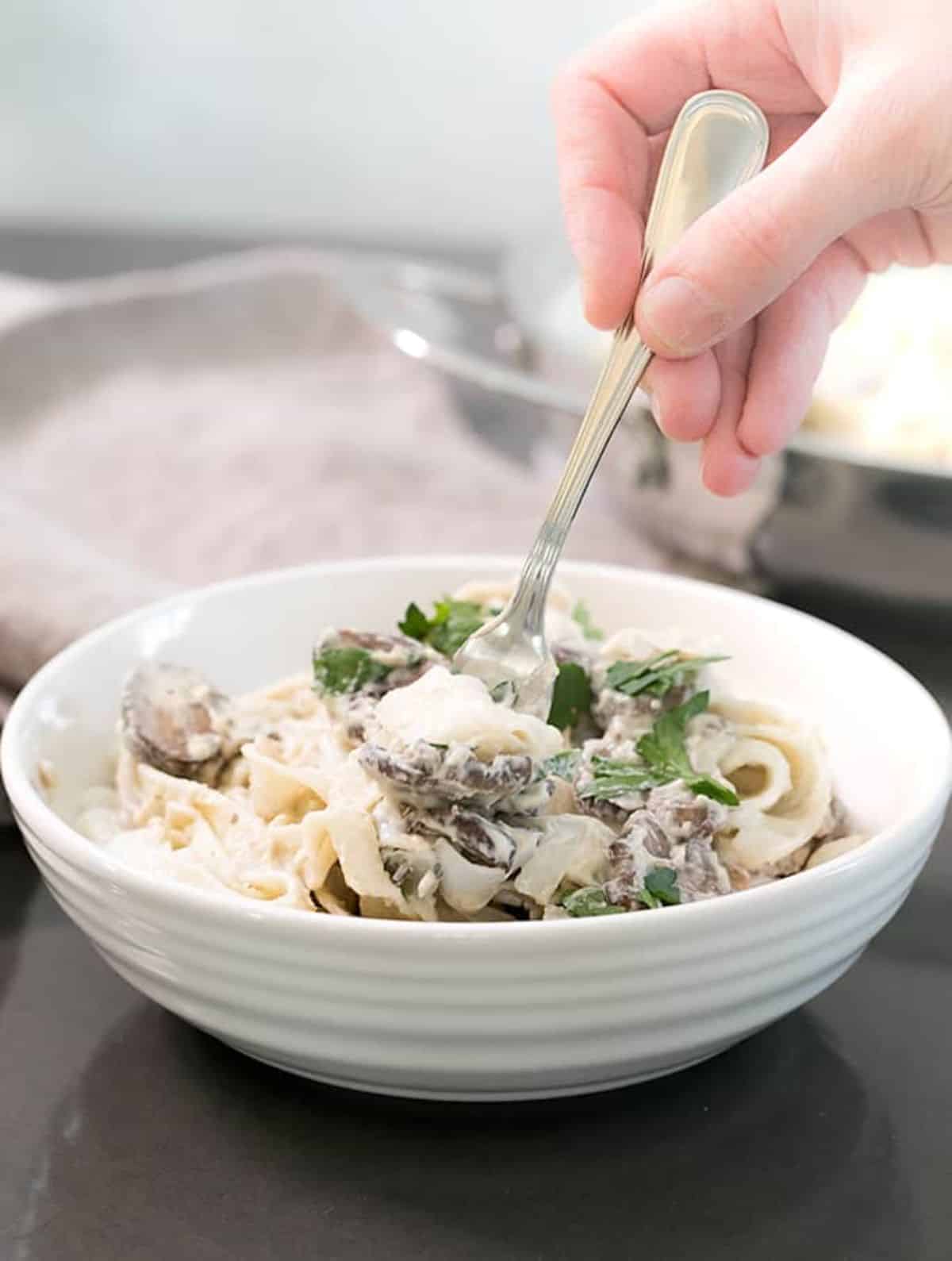 Easy Vegan Alfredo Sauce with Mushrooms and Pasta in a white bowl thwirled on a fork.